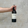 A hand holding a bottle of Port Askaig 28 Year Old Whisky against a grey concrete background.