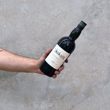 A hand holding a bottle of Port Askaig 45 Year Old Whisky with a concrete background.