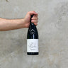 A hand holding a bottle of Château Pougelon 2020 Morgon wine against a concrete background.