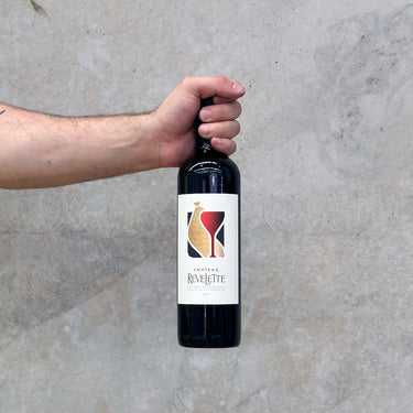 A hand holding a bottle of Château Revelette 2019 Château Red wine against a concrete background.