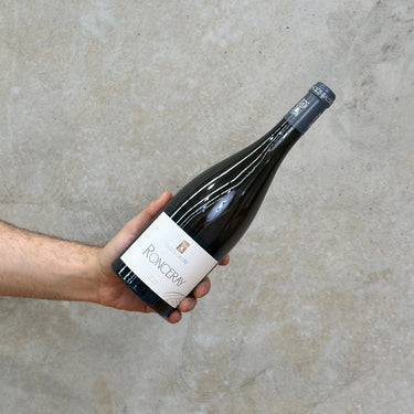 A hand holding a bottle of Le Clos Galerne 2022 Ronceray wine against a concrete wall.