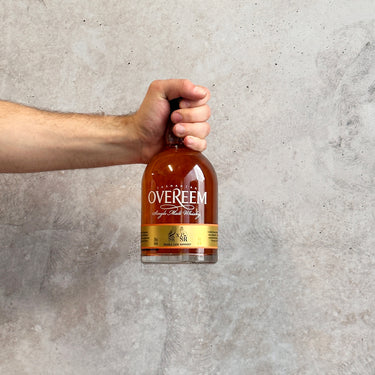 Hand holding a bottle of Overeem whisky against a gray background