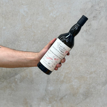 A hand holding a bottle of Glen Elgin Single Malts of Scotland Reserve Cask 13 Year Old Whisky against a grey concrete background.