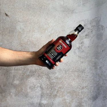 Hand holding a bottle of Springbank 10 Year Old PX Cask whiskey against a concrete wall