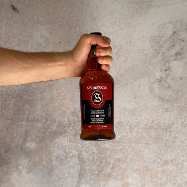 Hand holding a Springbank Palo Cortado Cask Matured Aged 10 Years whisky bottle against a concrete background