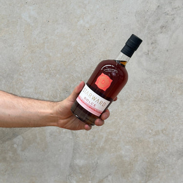 A hand holding a bottle of Starward Dolce Whisky with a concrete background.