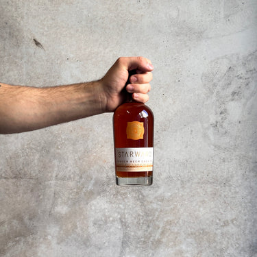 Hand holding a bottle of Starward ginger beer against a gray concrete background