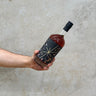 Hand holding a bottle Starboard Viotalis with a black label against a light stone background