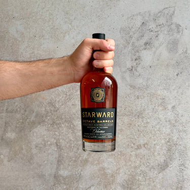 Hand holding a bottle of Starward whiskey against a gray concrete wall