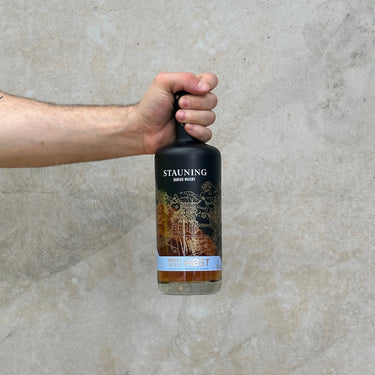 Hand holding a bottle of Stauning Danish Whisky, Smooth and Delicate Host against. concrete wall.