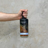 Hand holding a bottle of Stauning Danish Whisky, Smooth and Delicate Host against. concrete wall.
