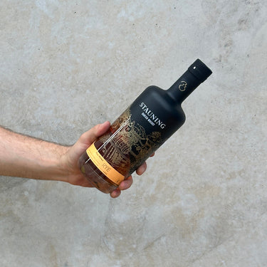 A hand holding a bottle of Stauning Rye Whisky with a decorative label, against a concrete background.