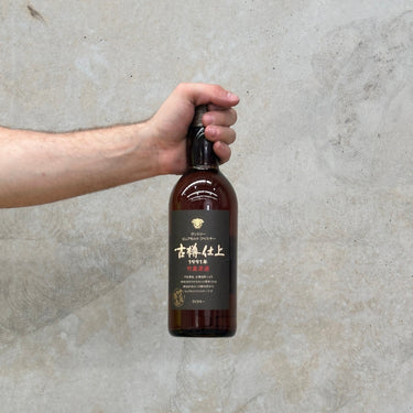 A hand holding a bottle of Suntory 1991 Furudaru Shiage Whisky against a grey concrete background.