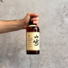 Hand holding a bottle of Suntory Pure Malt Whisky Aged 12 Years against a gray concrete background