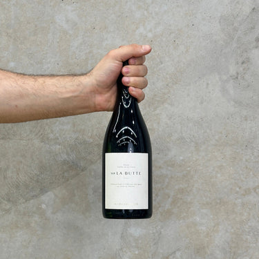 A hand holding a bottle of Château De Plaisance 2019 Sur La Butte wine, against a concrete wall. 
