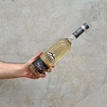 A hand holding a bottle of Terralta Extra Anejo Tequila against a grey concrete background.