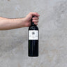 A hand holding a bottle of Terre Des Dame 2021 La Dame wine against a grey textured background.