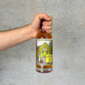 Hand holding a That Boutique-y Whisky Company bottle with a colorful label against a gray background