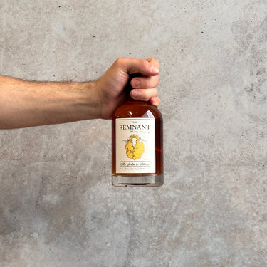 Hand holding a bottle of 'The Remnant' against a gray concrete wall