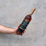 Hand holding a bottle of Francois Voyer Cognac against a concrete grey wall.