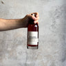 Hand holding a bottle of 'Waubs Harbour' against a gray concrete background