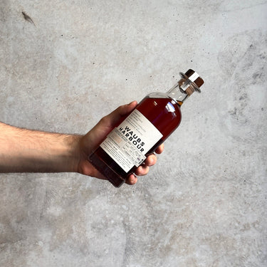 Hand holding a bottle of Waubs Harbour against a gray concrete background