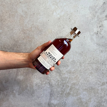 Hand holding a bottle of Waubs Harbour Rum Cask Tawny Limited Release against a concrete wall