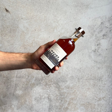 Hand holding a bottle of 'Waub's Harbour' Original against a gray concrete background