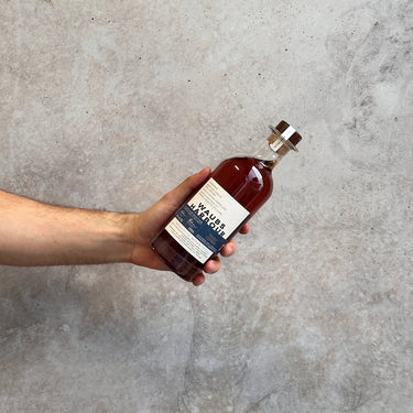 Hand holding a bottle of Waubs Harbour Port Storm whisky against a concrete wall