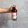 Hand holding a bottle of Waubs Harbour against a gray concrete background