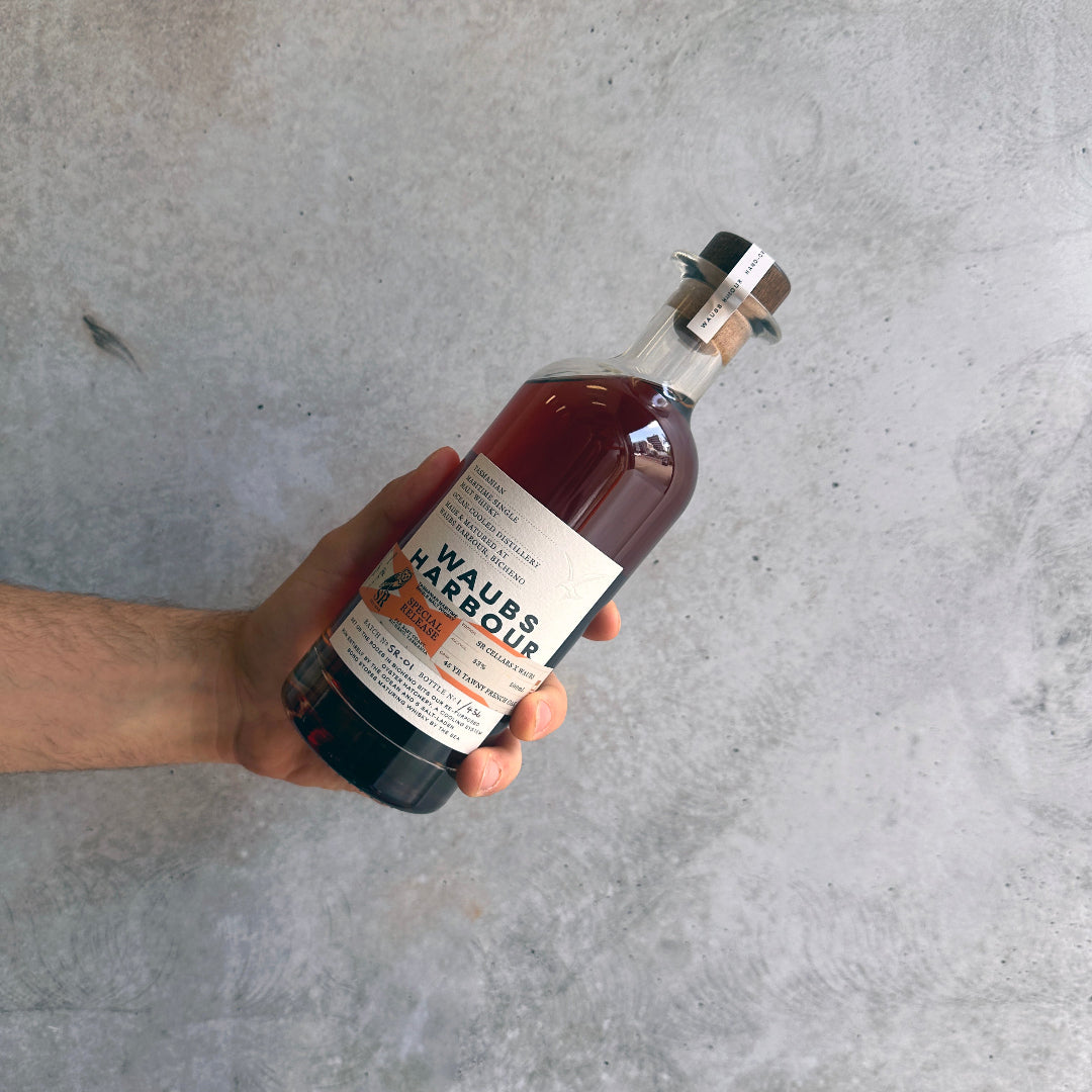 Hand holding a bottle of Waubs Harbour Savile Row and SR Cellars Private Collaboration against a concrete background