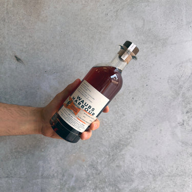 Hand holding a bottle of Waubs Harbour Savile Row and SR Cellars Private Collaboration against a concrete background