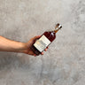 Hand holding a bottle of Waubs Harbour Stout Cask Whisky against a gray concrete background