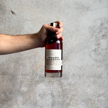 Hand holding a bottle of Waub's Harbours Yeast Cask against a gray concrete background