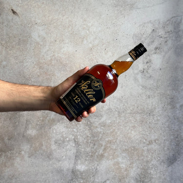 Hand holding a bottle of Weller 12 Year Old bourbon against a concrete background