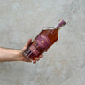 A hand holding a bottle of Westward Pinot Noir Cask Whisky against a grey concrete background.