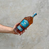 Hand holding a bottle of Westward Single Malt Whiskey against a concrete background