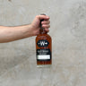 A hand holding a bottle of Westward Sourdough Whisky with a concrete background.