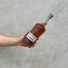 A hand holding a bottle of Wild Turkey 12 Year Old 101 Proof Whisky with a concrete background.