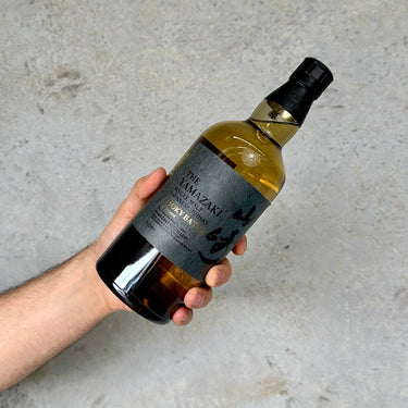 Hand holding a bottle of Yamazaki Smoky whisky against a gray background