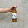 A hand holding a bottle of Yoichi 2021 Limited Edition Non-Peated Whisky against a textured grey background.