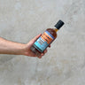 A hand holding a bottle of Ledaig 19 Year Old whisky with a label that includes the brand name, age, and volume information on a concrete background. That boutique-y whisky company