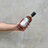 A hand holding a bottle of Adams 7 Year Old - Batch 1 whisky against a concrete wall